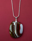 A sterling silver chain necklace with a fused glass pendant featuring a marbled pattern of reds and autumnal hues.
