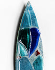 A close up of a fused glass surf board wall panel with mirror glass and mosaic inspired design. Handmade in marine blues, creating a lovely coastal piece of art work.