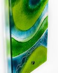 A close up of a fused glass wall panel in vibrant marine colours, in an abstract design. Hand-made in our Cornish studio.