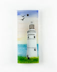 A fused glass extra small wall panel, featuring a lighthouse design with a very soft sunset pink sky, with soaring birds. A soft coastal piece of wall art.