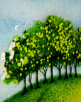 A fused glass depiction of trees on a hillside with a blue sky background