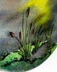 A close up of the grass detailing on a fused glass circular wall art panel featuring a hand-painted design of a fisherman in a small boat casting a line in front of a large glowing yellow sun over a calm lake in natural, organic colours.