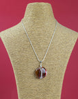 A sterling silver chain necklace with a fused glass pendant featuring a marbled pattern of bright reds and autumnal hues, seen on a mannequin