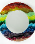 A circular fused glass round mirror in a vibrant rainbow colour-way with soft waves and textured detailing.
