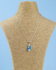 A sterling silver chain necklace with a teardrop-shaped fused glass pendant handmade featuring a ocean blue marbled design seen on a mannequin.