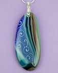 Close up of fused glass pendant necklace, handmade in coastal hue, with an organic, swirling hand-painted design.
