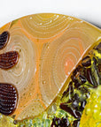 Hand-painted detailing on a fused glass round panel featuring organic autumn inspired patterns and shapes, in a vibrant yellow colour-way, handmade and inspired by the autumnal season.