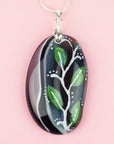 Close up of fused glass pendant necklace, handmade in spring greens and pinks, with botanical hand-painted design.