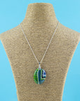 Fused glass pendant necklace, with hand-painted dots and swirls, in an ocean blue and green colour-way. Pendant is hung on a sterling silver chain.
