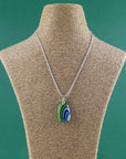 An artisan fused glass pendant necklace in coastal blues and greens, handcrafted in our studio. Finished with a sterling silver chain and fittings, a striking piece of wearable art. Shown on a mannequin.