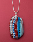 An extra large fused glass pendant necklace, handmade in rosey red and coastal blue hues, with hand-painted patterns and hung on a sterling silver chain