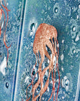Close up of fused glass staggered triptych, handmade using copper, which has been hand etched into an intricate Jellyfish design, with bubbled marine blue background.