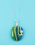 Fused glass pendant necklace, with hand-painted dots and swirls, in an ocean blue and green colour-way. Pendant is hung on a sterling silver chain.