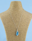 A fused glass pendant necklace, handmade in aqua blue hues, hung on a sterling silver chain.
