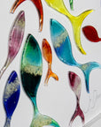 Close up of signed signature and Individually hand-cut fused glass fish in rainbow hues on a white art frame.