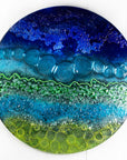 Fused glass round wall panel in an abstract ocean inspired design with textured detail.