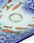 Bubbled detail of fused glass square dish, handmade in coastal blues, with copper fish.