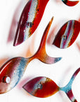 Close up o fused glass shoal of fish in bright reds and aqua hues, with shadows.