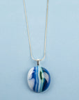 Close up of fused glass pendant necklace, handmade in coastal blues, hung on a sterling silver chain.