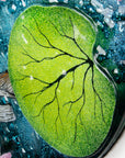 Leaf details on a fused glass round panel featuring hand-painted koi carp design with waterlilies and marine blue background.