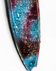 A close up of fused glass surfboard wall panel, handmade in coral pink hues and ocean blues, with textural detailing. A coastal inspired piece of wall art.