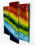 Side view of fused glass staggered triptych in bright rainbow colours, placed onto mirror glass. A vibrant piece of wall art.