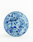 A fused glass round dish, handmade using recycled marine blue hues, designed to create a striking, ocean inspired piece of decor.