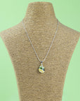 A sterling silver chain necklace with a teardrop-shaped fused glass pendant handmade featuring a golden yellow and sea greens in a marbled design seen on a mannequin.