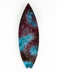 A fused glass surfboard wall panel, handmade in coral pink hues and ocean blues, with textural detailing. A coastal inspired piece of wall art.