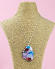 A sterling silver chain necklace with a fused glass pendant featuring a marbled pattern of soft pinks and delicate blue and red hues, seen on a mannequin.