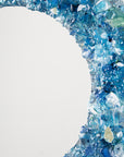 A close up of a fused glass round mirror, handmade using recycled crushed glass in ocean blue hues, with lots of organic texture.
