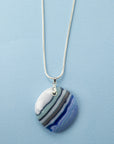 A sterling silver chain necklace with a fused glass pendant featuring a marbled pattern of coastal blues and white.