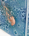 Detailing of fused glass staggered triptych, handmade using copper, which has been hand etched into an intricate Jellyfish design, with bubbled marine blue background.
