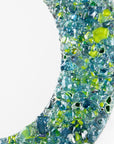 A close up of a fused glass round mirror, handmade using recycled ocean coloured glass in green and aqua hues. A coastal inspired piece of wall art.