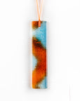A fused glass hanging, hand-coloured in vibrant orange and bright aqua tones, with an orange ribbon.