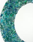 A close up of a fused glass round mirror handmade using crushed, recycled glass to create an ocean inspired piece of wall art.