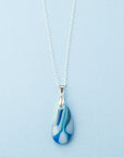 A fused glass pendant necklace, handmade in aqua blue hues, hung on a sterling silver chain.