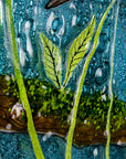 Close up of leaf on a round fused glass wall panel, with hand-painted kingfisher design in vibrant organic colours and textures.