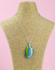 A sterling silver chain necklace with a fused glass pendant featuring a marbled swirl pattern of green, blue, and blushed white, seen on a mannequin.