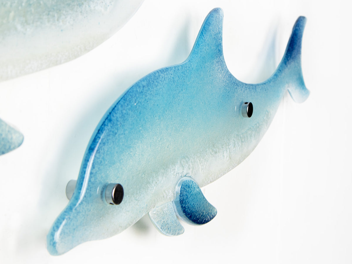 A close up of the smaller dolphin from a pair, handmade in fused glass, designed in soft coastal blues and whites. 