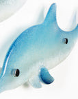 A close up of the smaller dolphin from a pair, handmade in fused glass, designed in soft coastal blues and whites. 