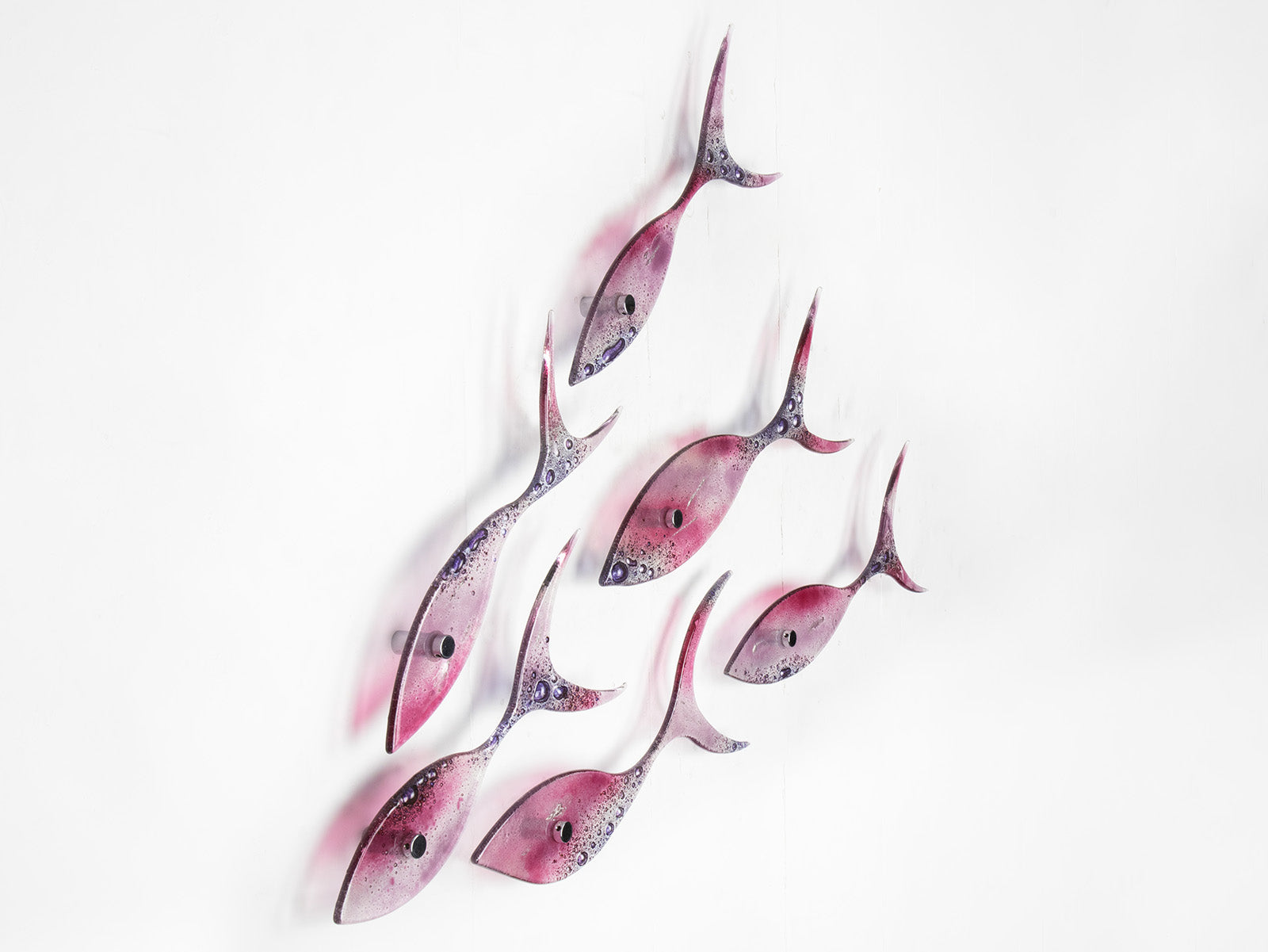 A fused glass shoal of fish, with individual fish installed in a bright pink and bubbled purple colour-way. 