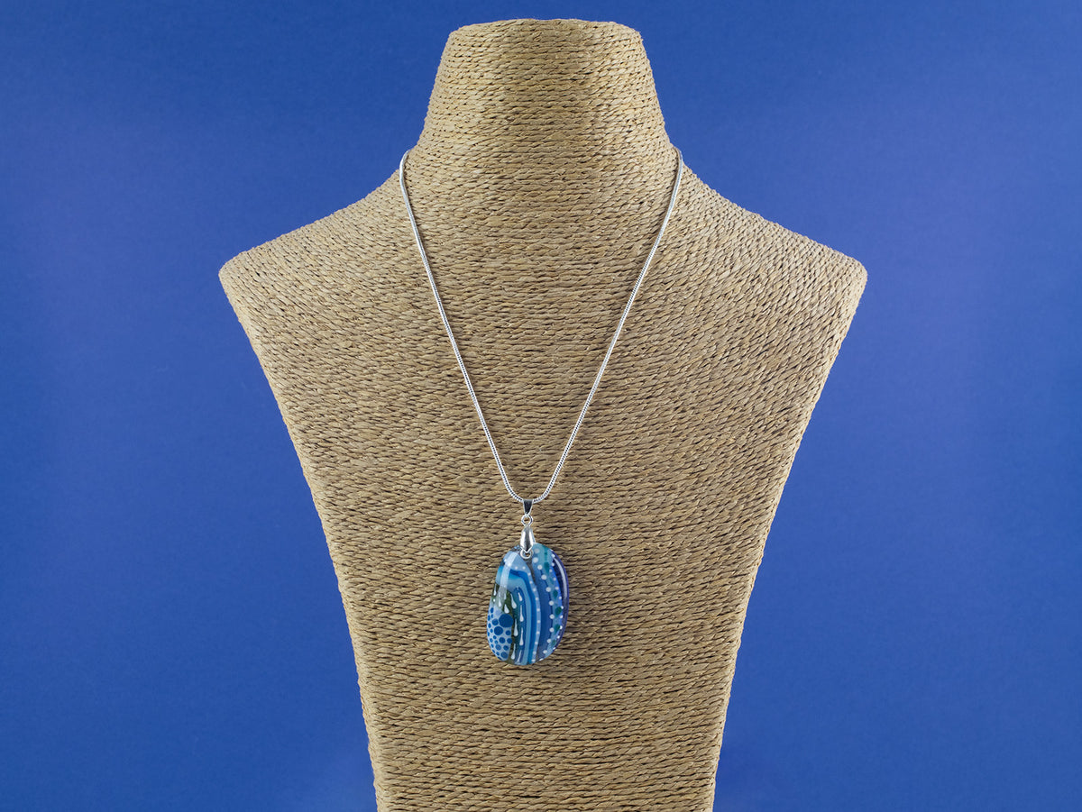 A signature by Jo Downs fused glass pendant necklace handmade using some of Jo's innovative techniques in rich ocean blues. Finished with a sterling silver chain and fittings, shown on a mannequin. 