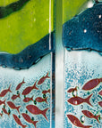A close up of a fused glass triptych featuring marine blues and greens in an ocean design, with copper fish and textured detail. 