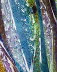 A close up or organic texture on a fused glass wall panel, featuring a wavy design in sea blues, greens and amethyst purples with textured detailing. 