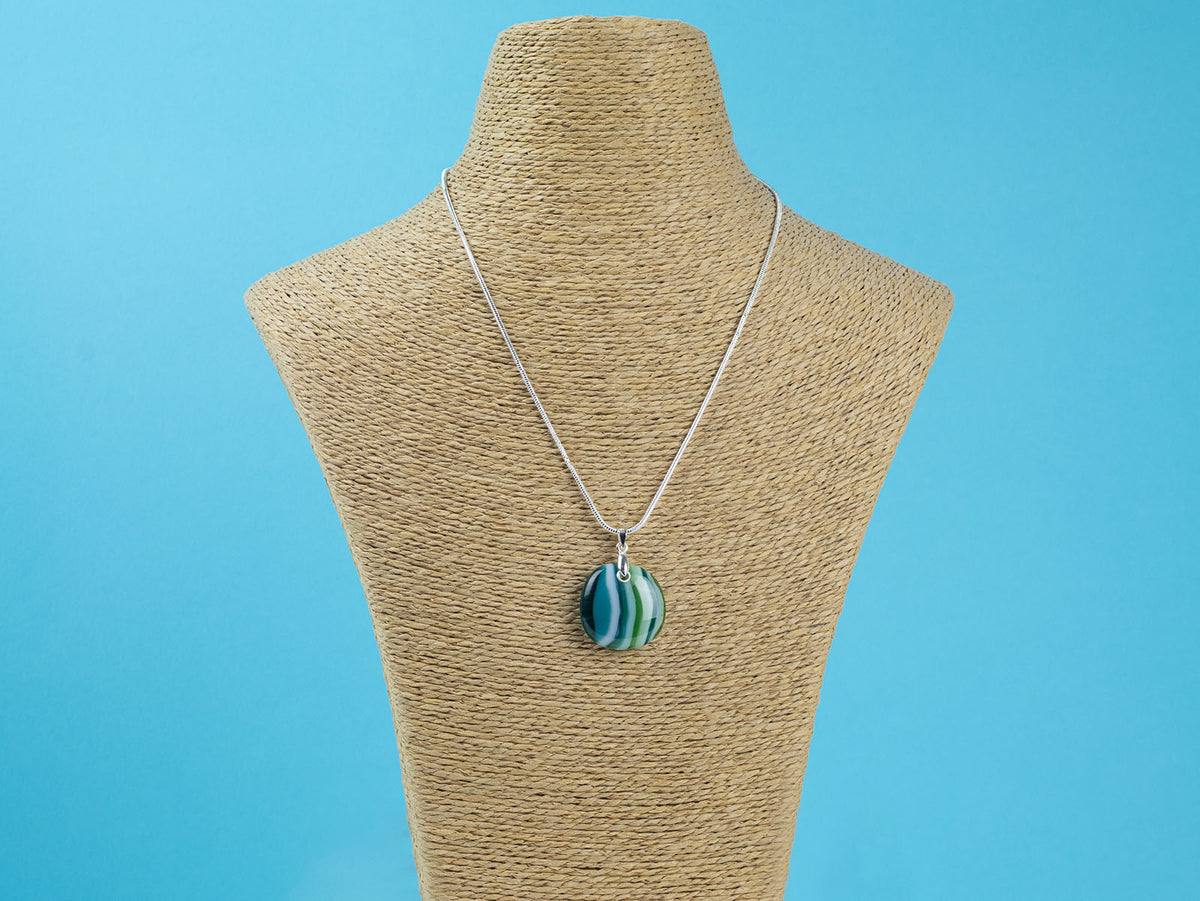 A sterling silver chain necklace with a round fused glass pendant featuring green, teal, and white wavy stripes, handmade in coastal colours and seen on a mannequin. 