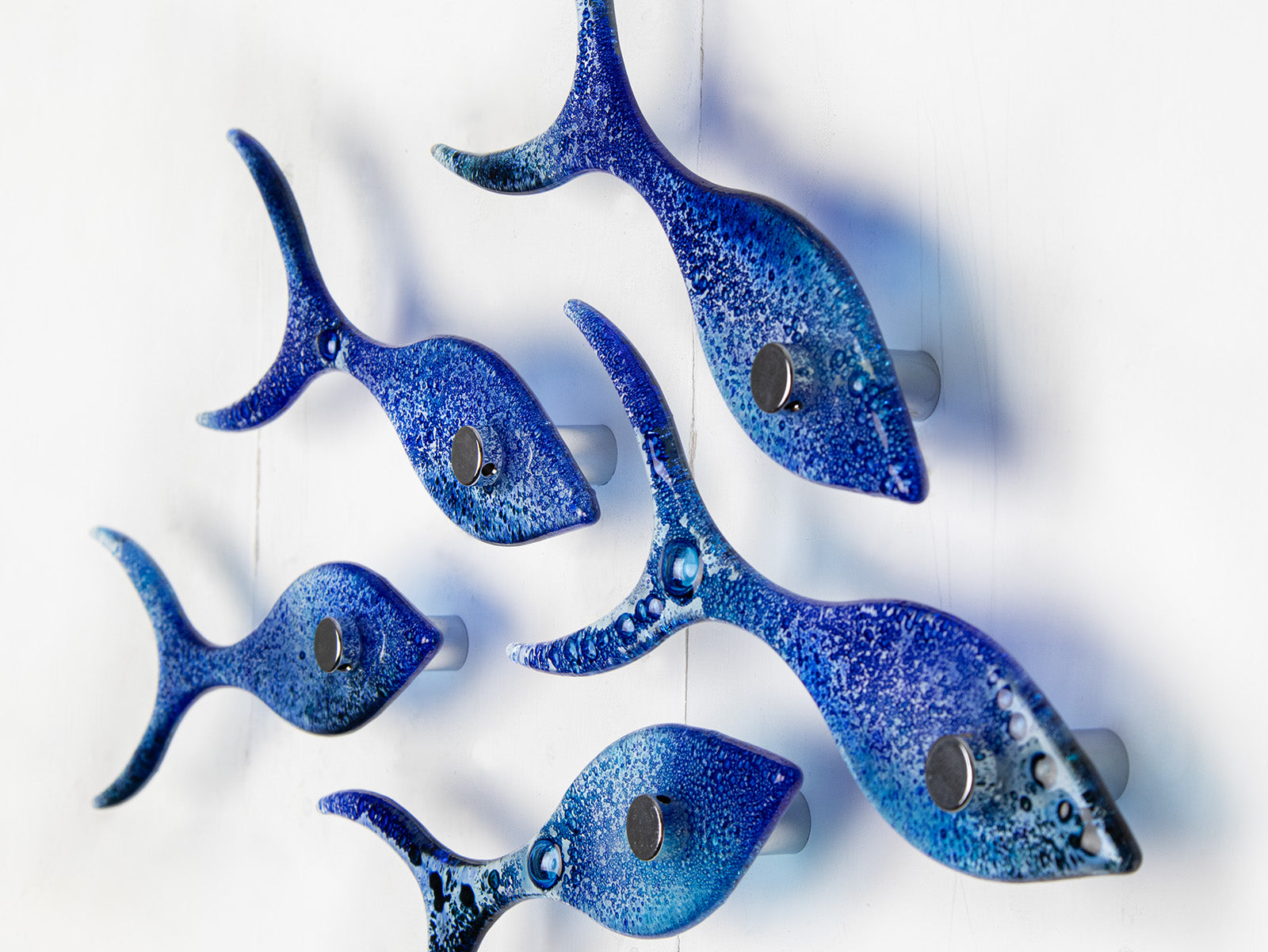 Close up of small fused glass shoal of fish, handmade in coastal blue colours with organic bubbled detailing. 