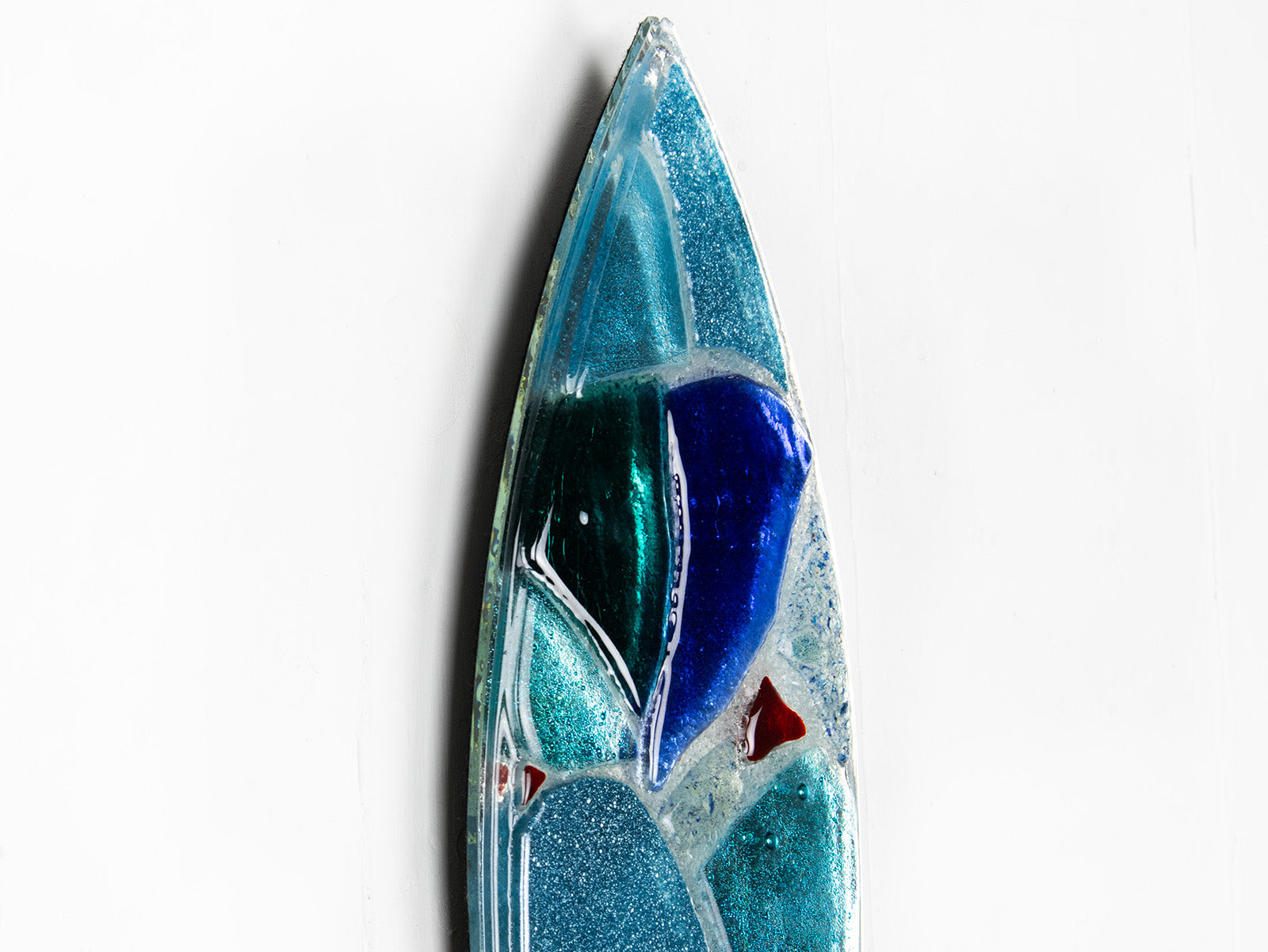 A close up of a fused glass surf board wall panel with mirror glass and mosaic inspired design. Handmade in marine blues, creating a lovely coastal piece of art work. 