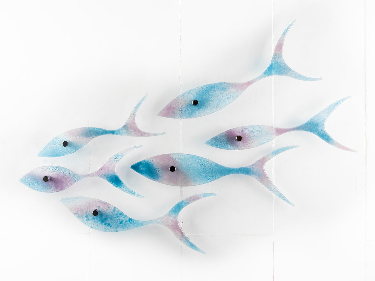 Fused glass shoal of fish in soft aqua and rose pink hues, creating an ocean inspired wall art installation. 