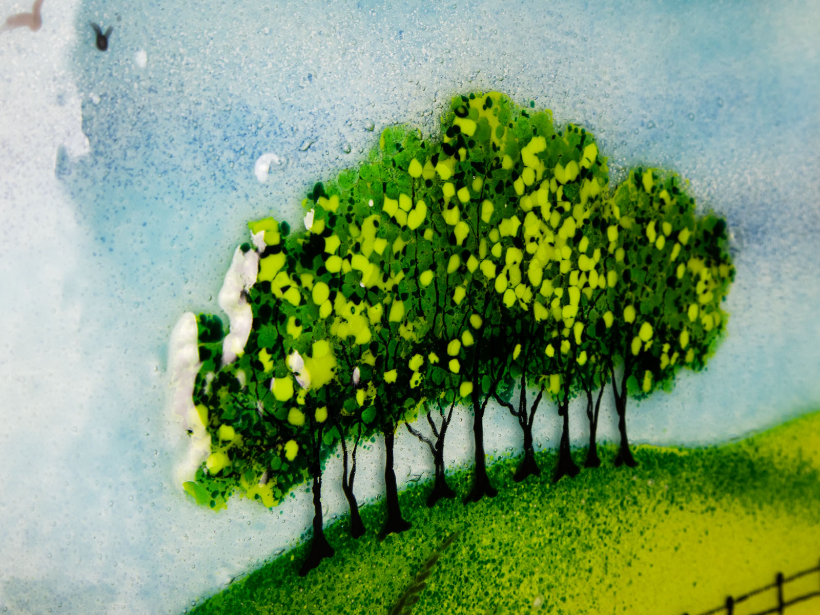 A fused glass depiction of trees on a hillside with a blue sky background